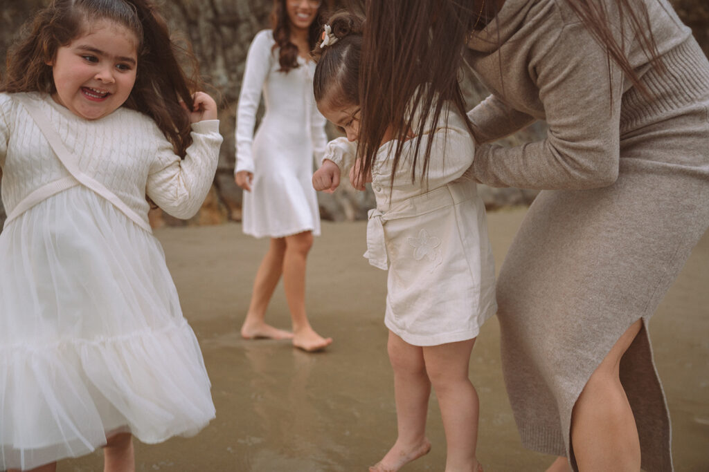 Two young girls play and splash in the shallow water at Crescent Bay as their family gathers behind them on the sand.