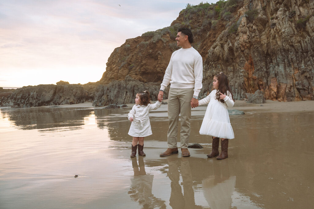 A father and his two young daughters stroll across the wet sand at Crescent Bay Beach, enjoying a calm moment at Laguna.