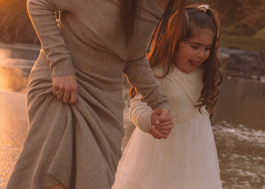 A close-up moment of a mother holding her daughter’s hand while they walk through the shallow tide at Crescent Bay in South Orange County.