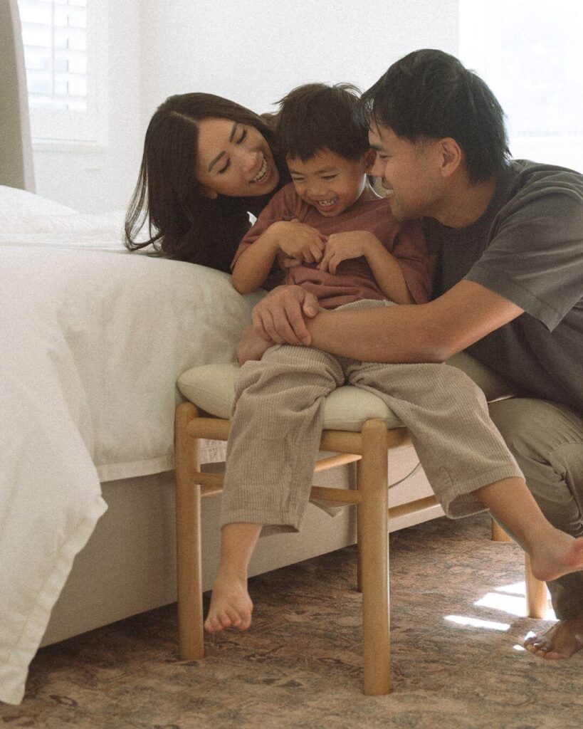 Parents laughing with their son while seated on a bedroom bench during an family session in orange county.
