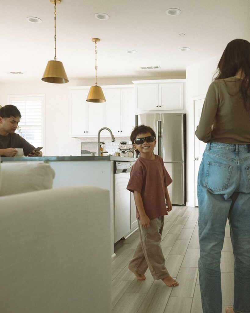 A young boy wearing sunglasses and smiling in the kitchen during a candid at-home family session in Irvine.