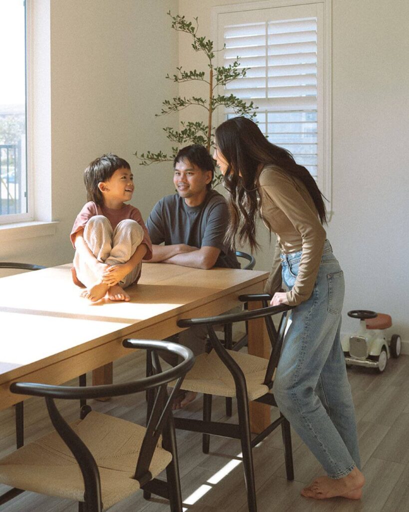 A family gathered around their dining table in their home, talking and smiling in warm morning light.