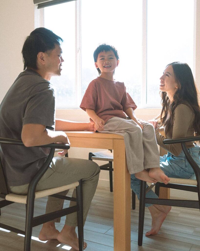 A mom and child in the kitchen while the dad sits at the dining table during a sunlit Irvine family session.