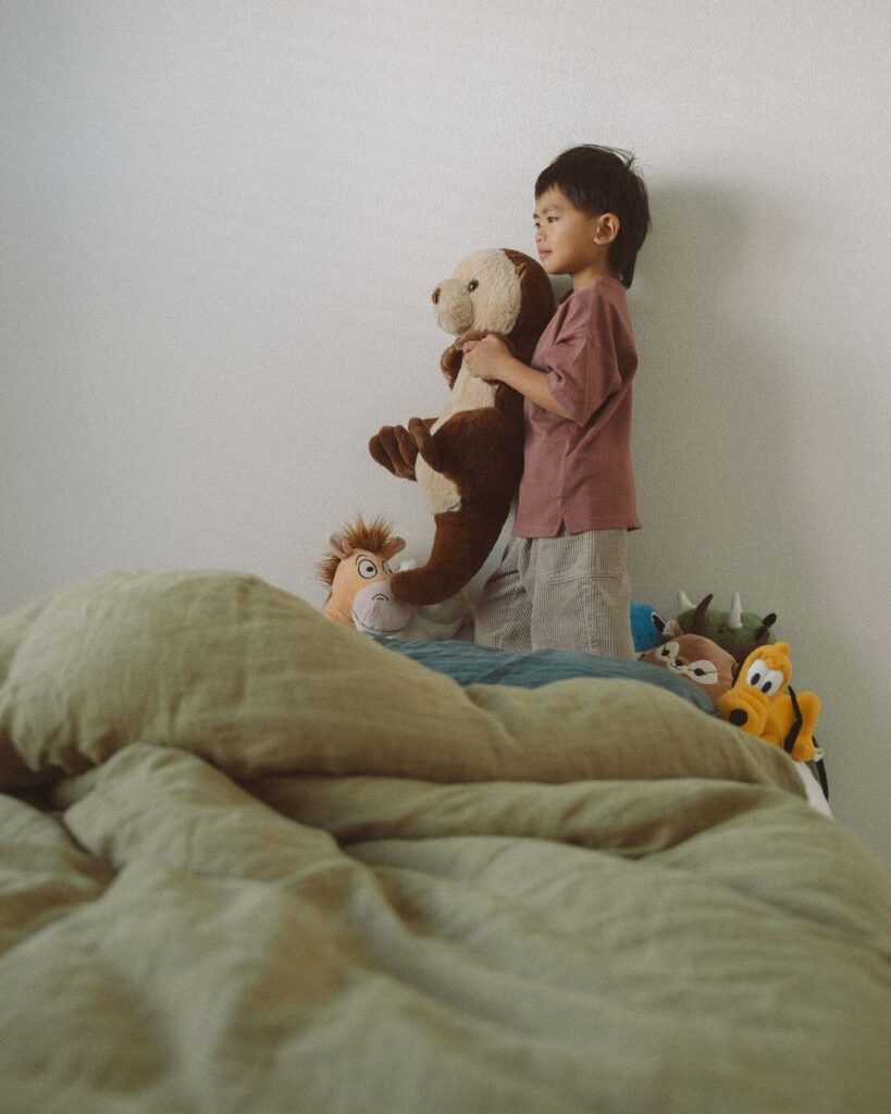 A young boy standing in his bedroom holding a stuffed animal during an at-home family session in Irvine, California.