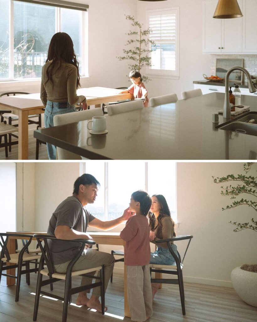 A mom and child in the kitchen while the dad sits at the dining table during a sunlit family photoshoot.