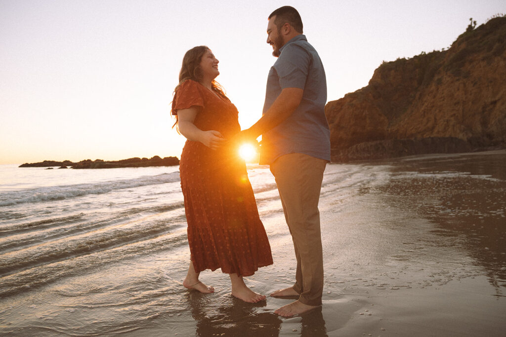 Couple standing together after their engagement in California, reflected in the wet sand at sunset.