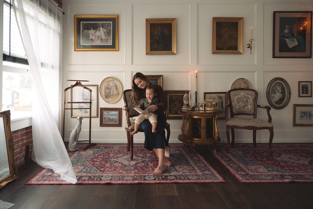 Wide editorial view of a mother and baby surrounded by artwork and soft light, creating timeless yet natural family photos.