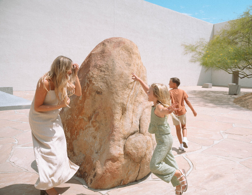 A mother and her children playing together outdoors in soft light, surrounded by warm neutral tones.