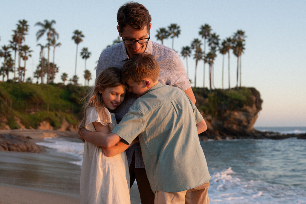 dad hugging kids at golden hour on Laguna Beach — Orange County family photographer Maria Alcantara