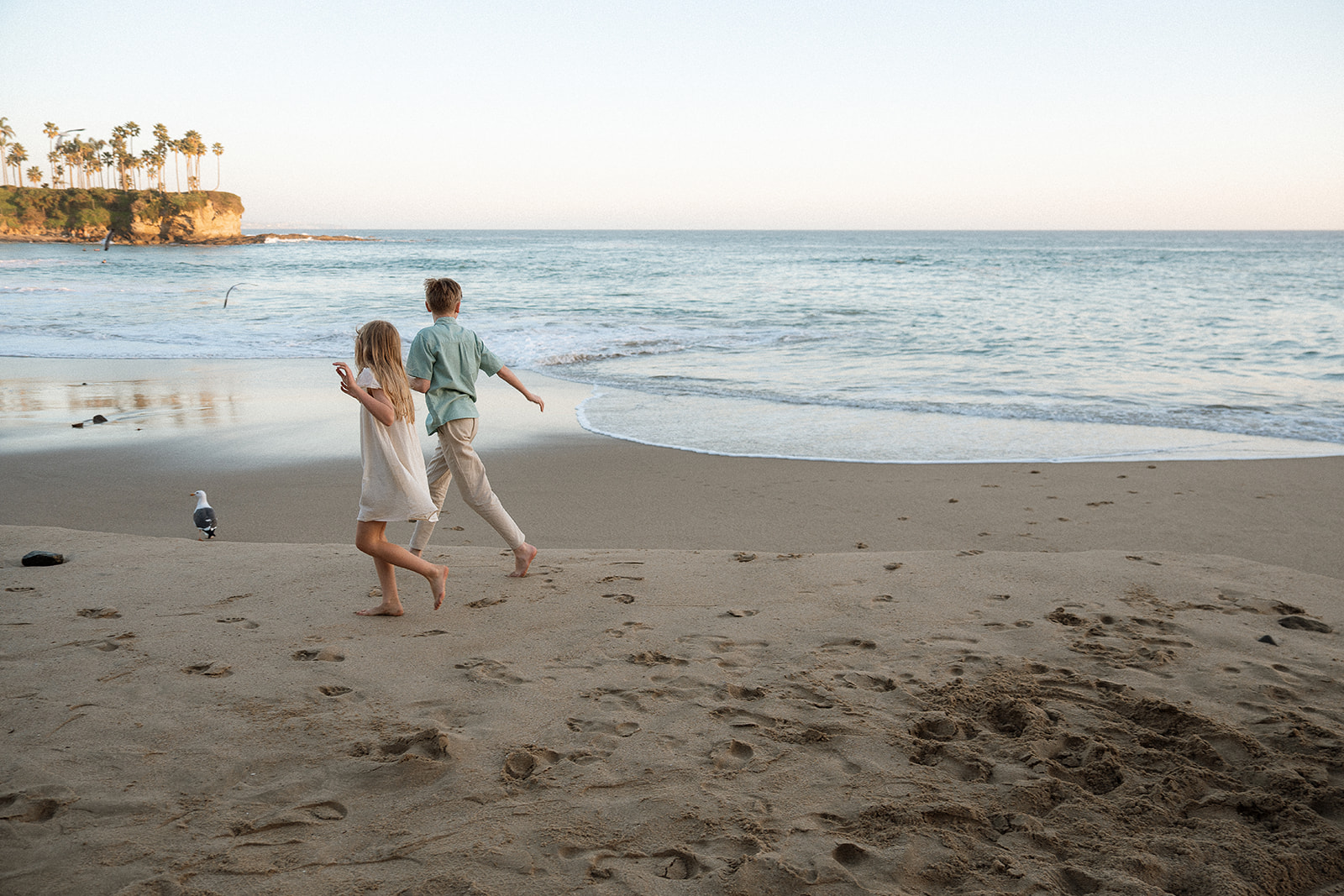Siblings running toward the water at Crescent Bay Laguna Beach — candid family photography by Maria Alcantara