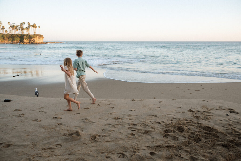 Siblings running toward the water at Crescent Bay Laguna Beach — candid family photography by Maria Alcantara