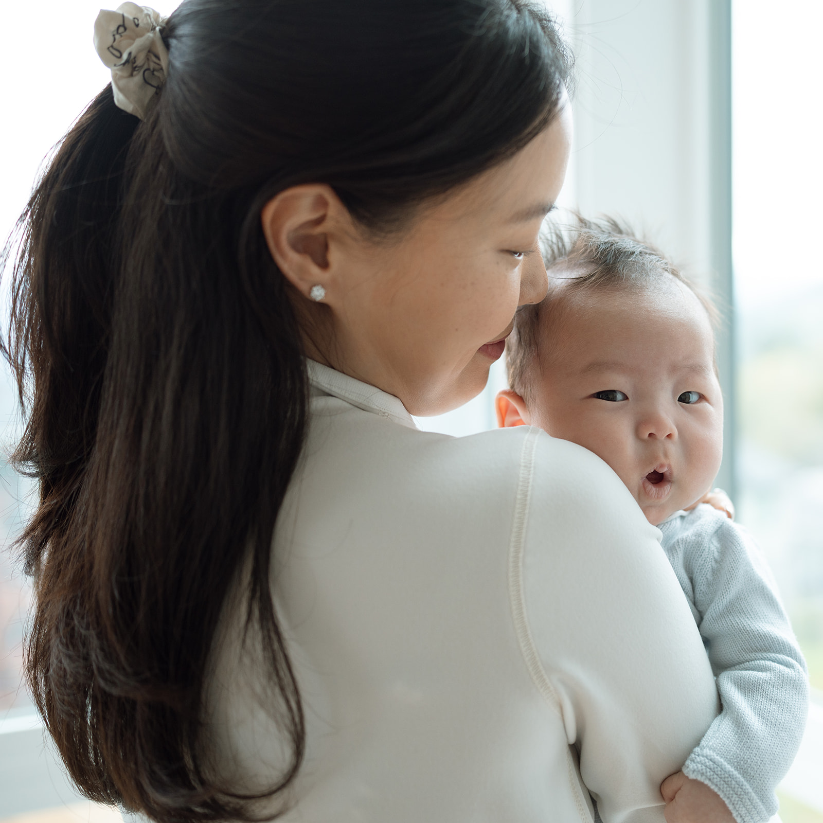 Mother nuzzling newborn in soft window light during at-home family session, Orange County photographer