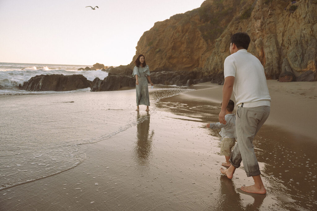 Candid moment of dad and toddler walking toward mom along the shoreline at Crescent Bay Beach from Laguna Beach family photographer