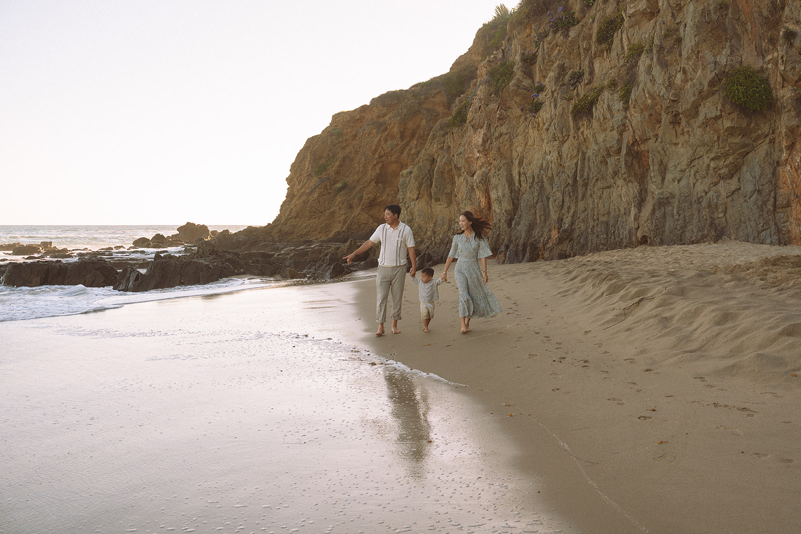 Laguna Beach family photographer captures a family of three walking along Crescent Bay Beach at golden hour