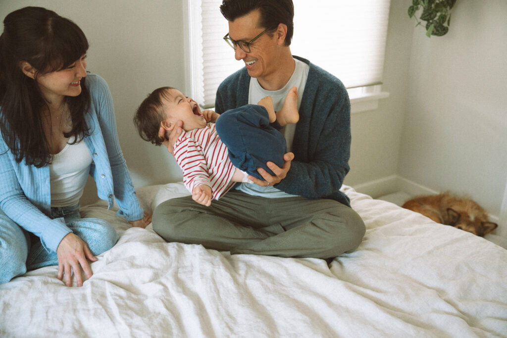 Father playfully holding toddler on the bed while mother laughs beside them, documentary family session