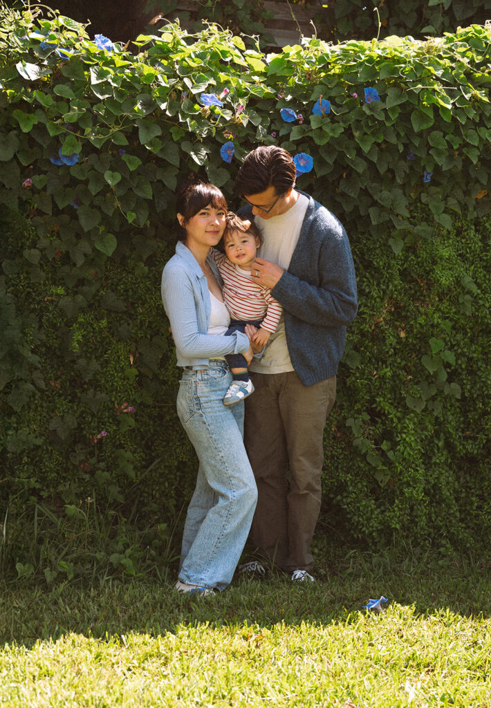 Mother and father holding toddler in front of a morning glory vine wall during an outdoor family portrait in Long Beach