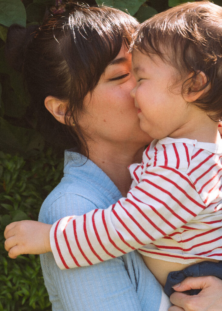Mother nuzzling her toddler close with eyes closed, garden background