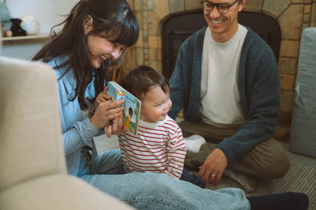 Parents read a Baby Giraffe board book with their toddler in front of a stone fireplace during an in-home lifestyle family session.