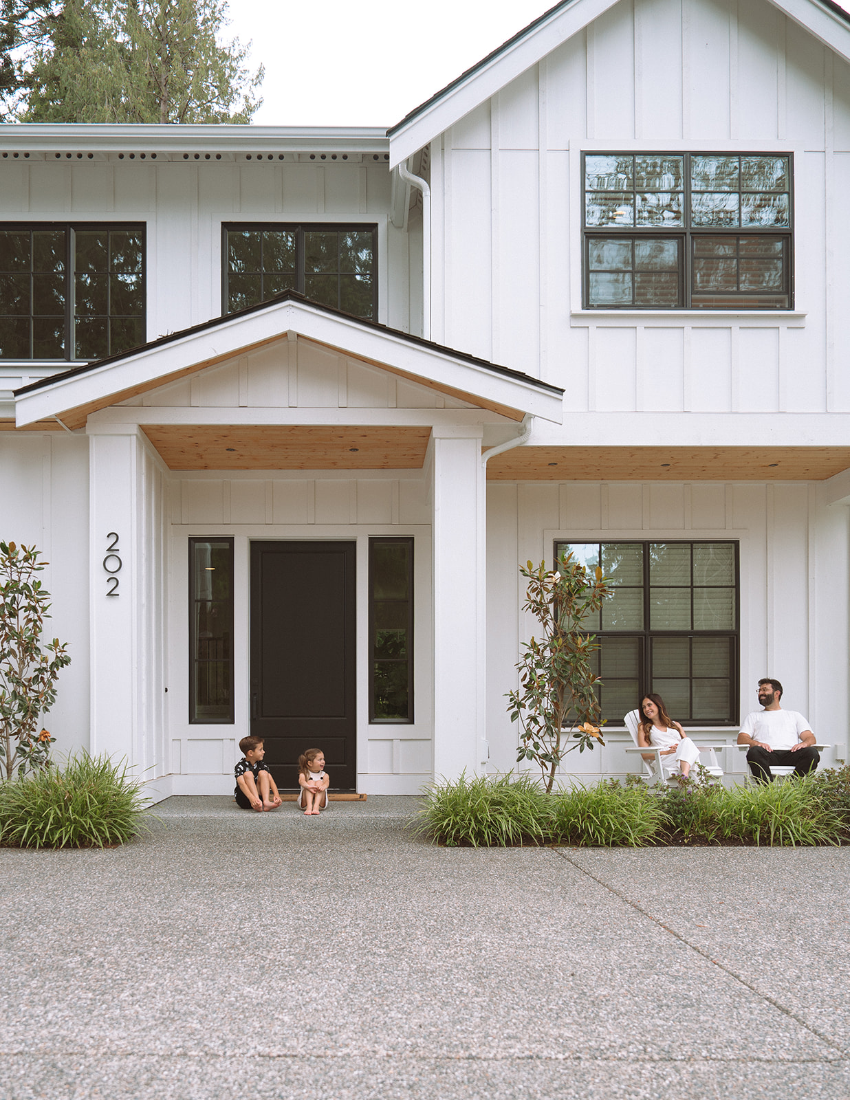 Family of four relaxes on the front porch of their modern white farmhouse during an at-home family session in Orange County.
