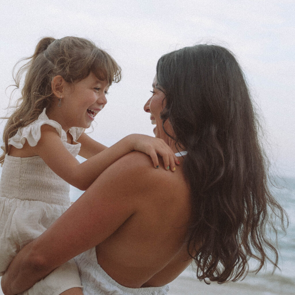 Mom holds her laughing daughter face to face during a beach family session in Laguna Beach, Orange County.