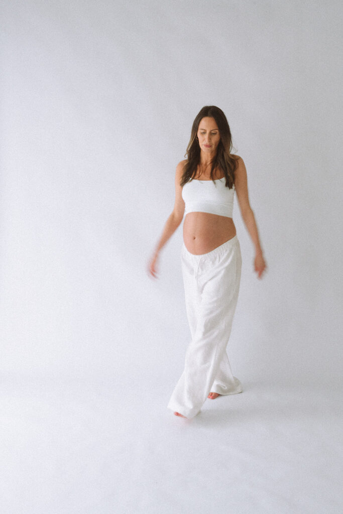 A mom-to-be mid-step across a bright white studio. A maternity studio session in orange county.