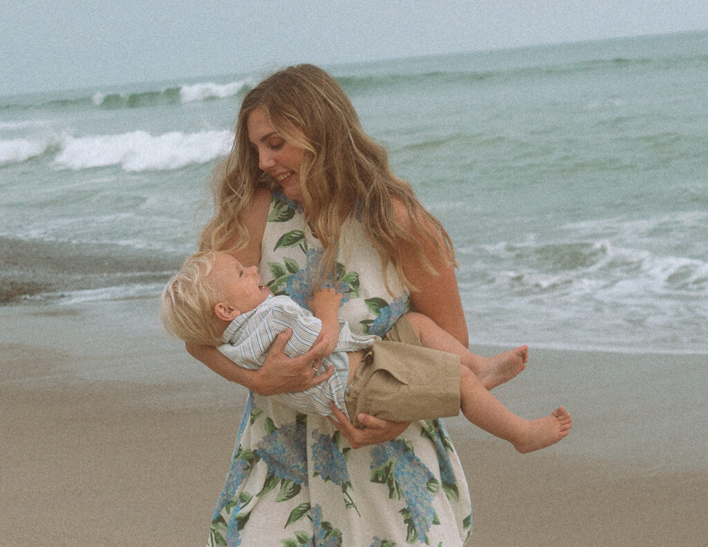 Mother cradling her toddler son and smiling down at him during a beach session in Orange County.