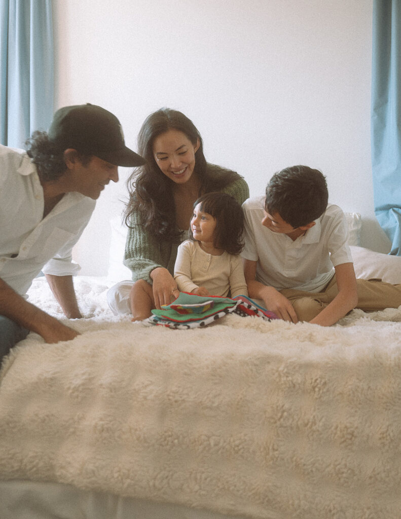 Whole family gathered on the bed reading a book together, baby smiling up at dad. Irvine lifestyle family photography.