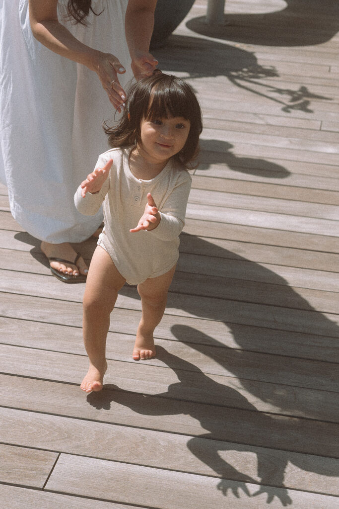 Barefoot toddler on a wooden deck, shadow stretching out behind her.