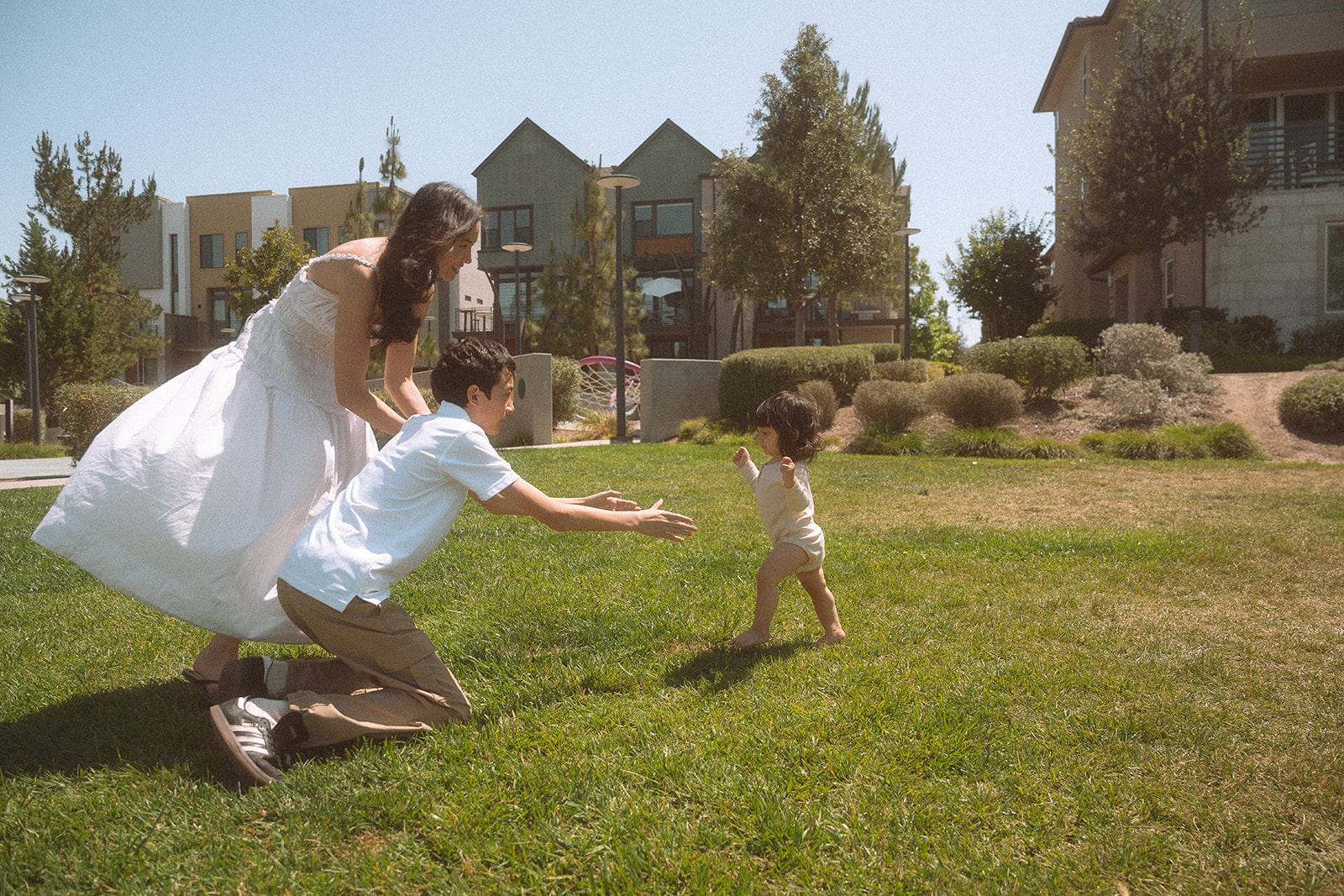 Big brother reaching out as baby sister runs across the grass toward him.