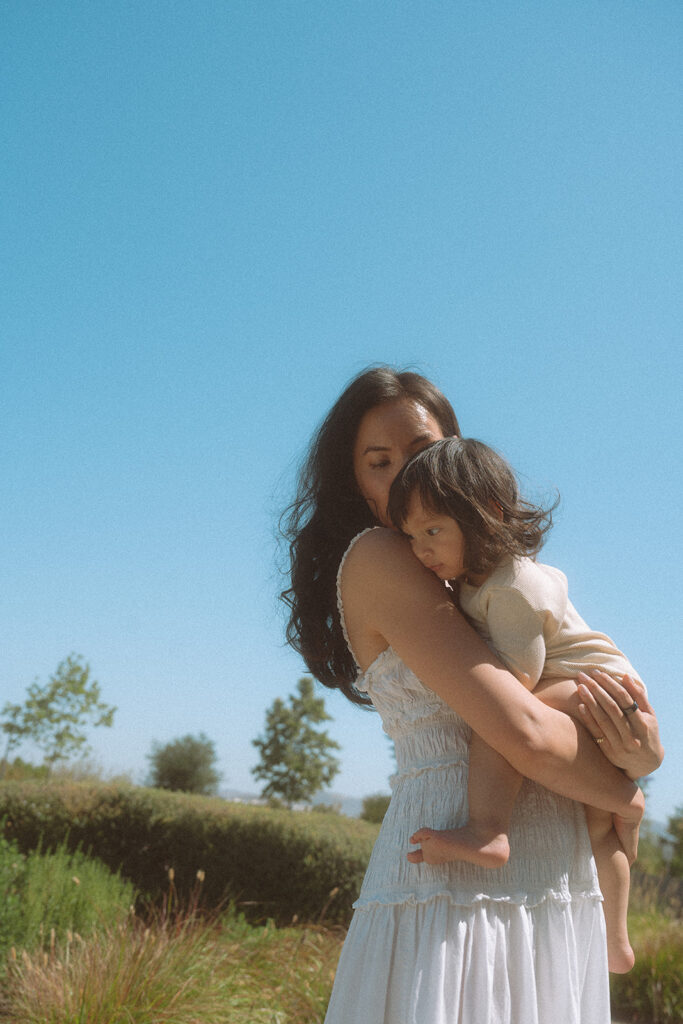 Mom holding her baby close against a clear blue sky.