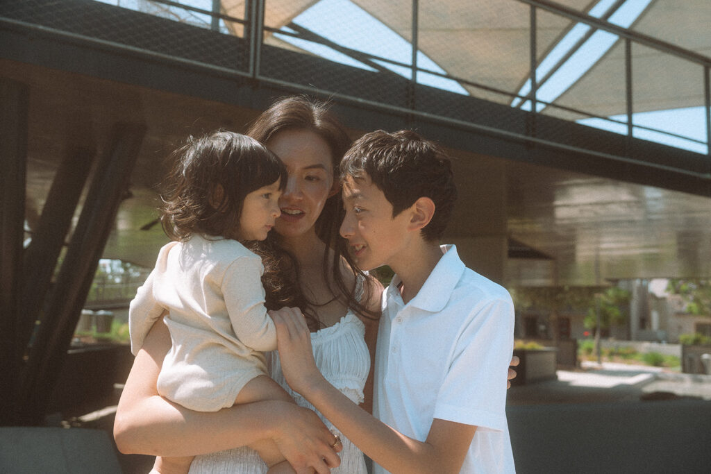 Irvine lifestyle family photography. Mom holding both kids close at an outdoor location.