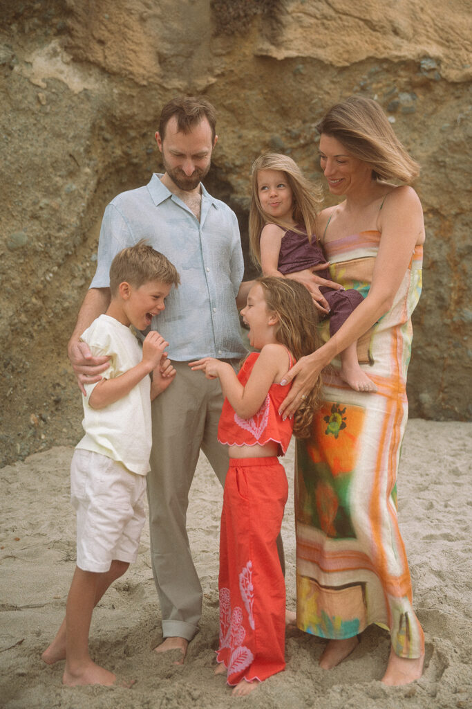Family of five laughs together against the cove's rock wall during a Victoria Beach family session in Laguna.