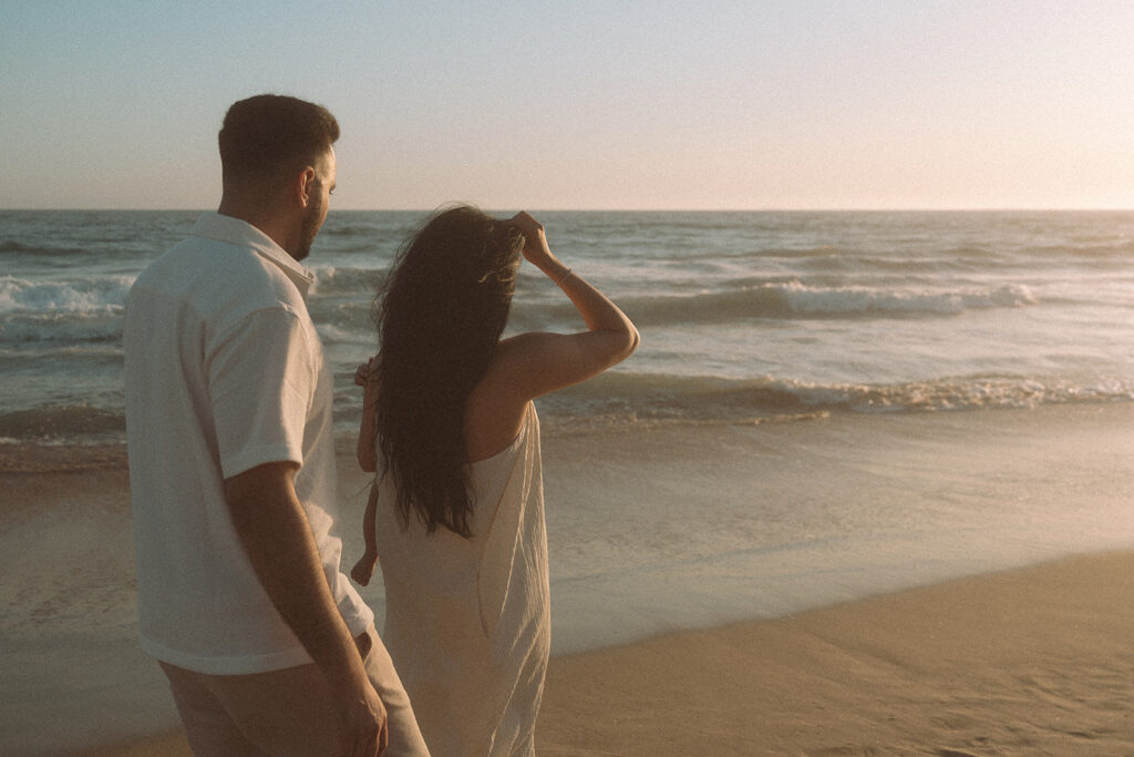 Parents walking together while holding baby on Newport Beach shoreline.