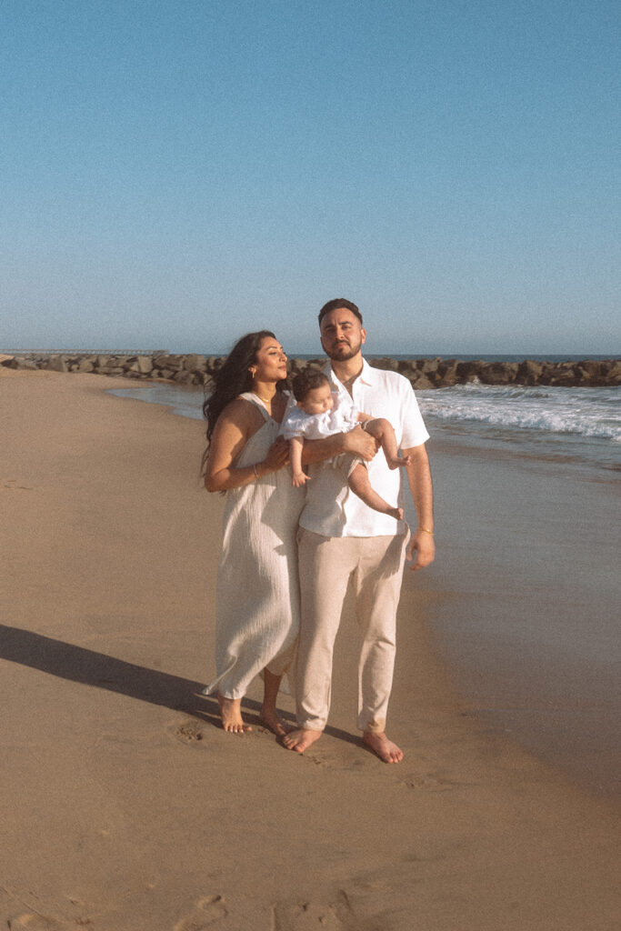 Family of three posing together on Newport Beach sand with jetty in the background.