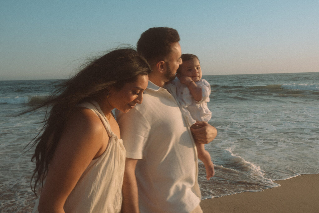 Family of three walking along beach shoreline during windy golden hour session.