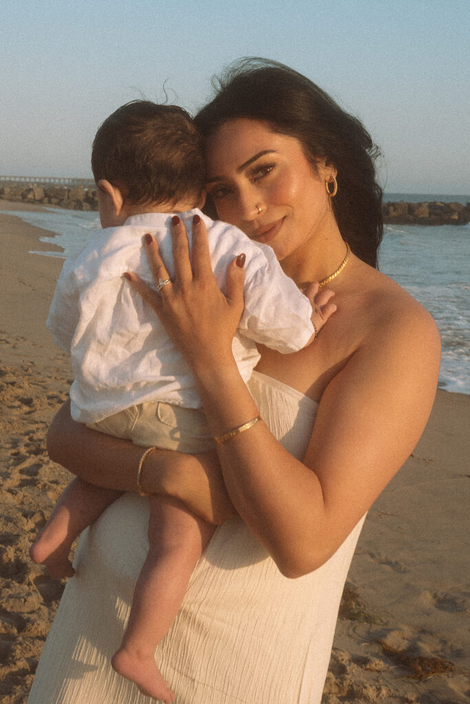 Mom holding baby against her cheek, smiling softly at camera during golden hour Newport Beach family session.