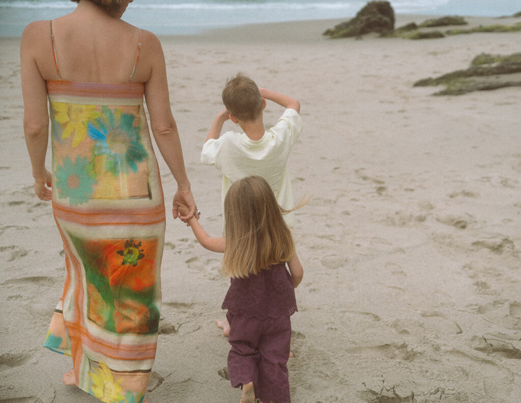 Mom walks hand in hand with her two children toward the rocks during a Victoria Beach family session in Laguna.