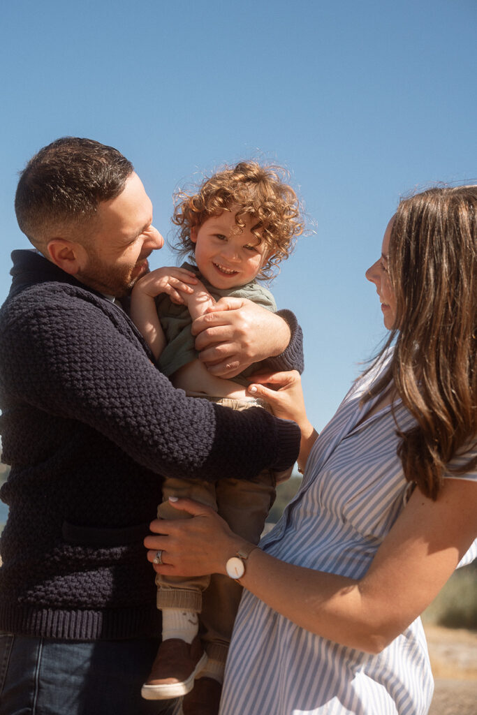 Parents holding up curly haired son bright blue skies at beach