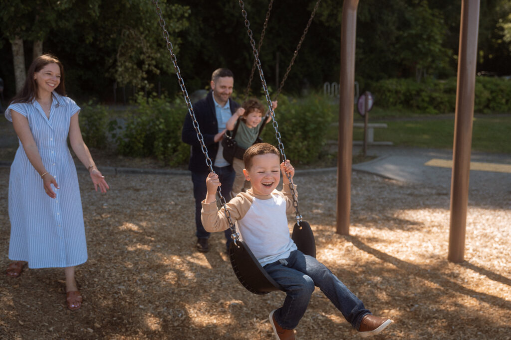 Child laughing on swing with parents engaged nearby - candid playful family photos