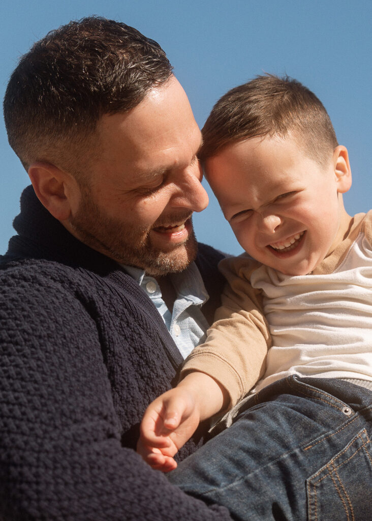 Father holding toddler son against bright blue sky at beach