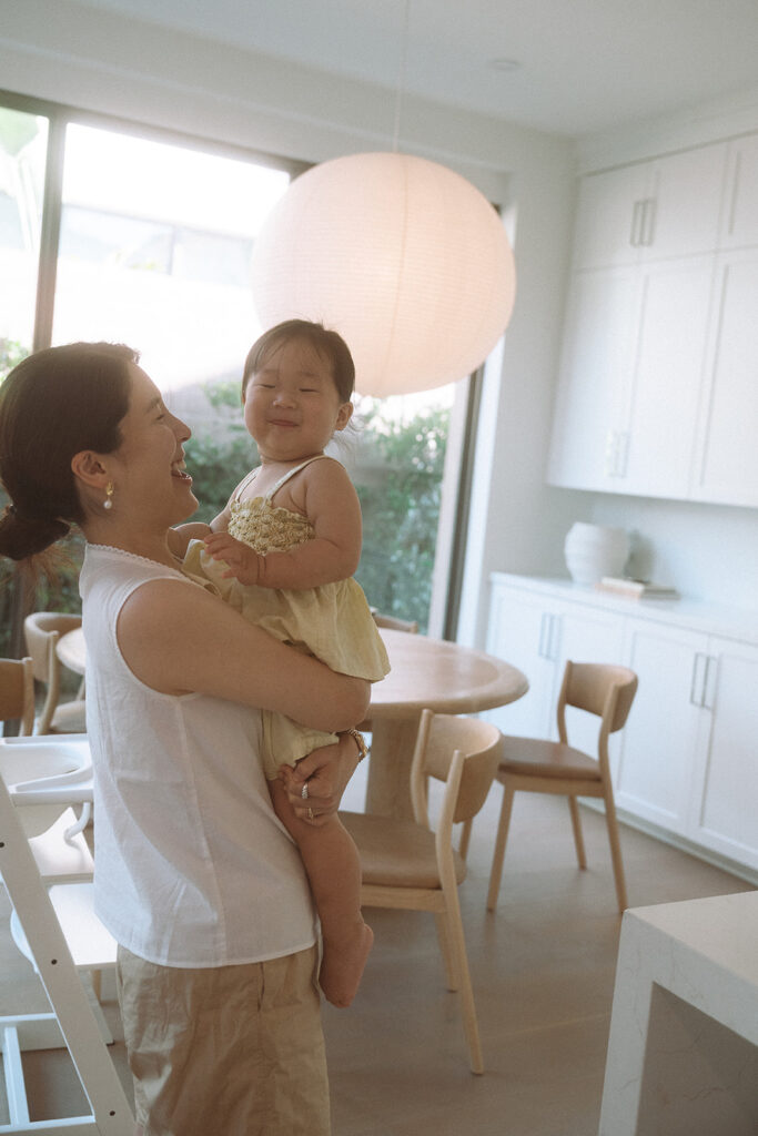 Mother carrying daughter through bright modern kitchen
