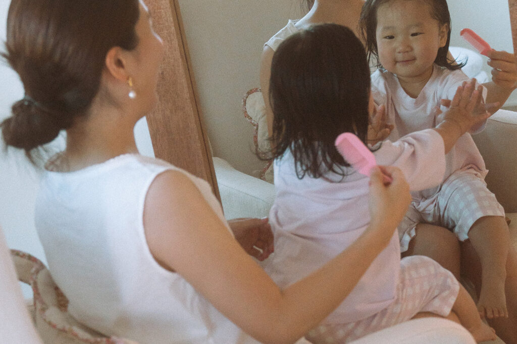 Toddler girl playing with hairbrush in mirror at home with mom