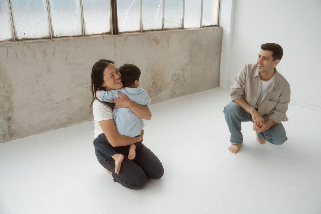 Father crouching beside mother holding child in studio family portrait