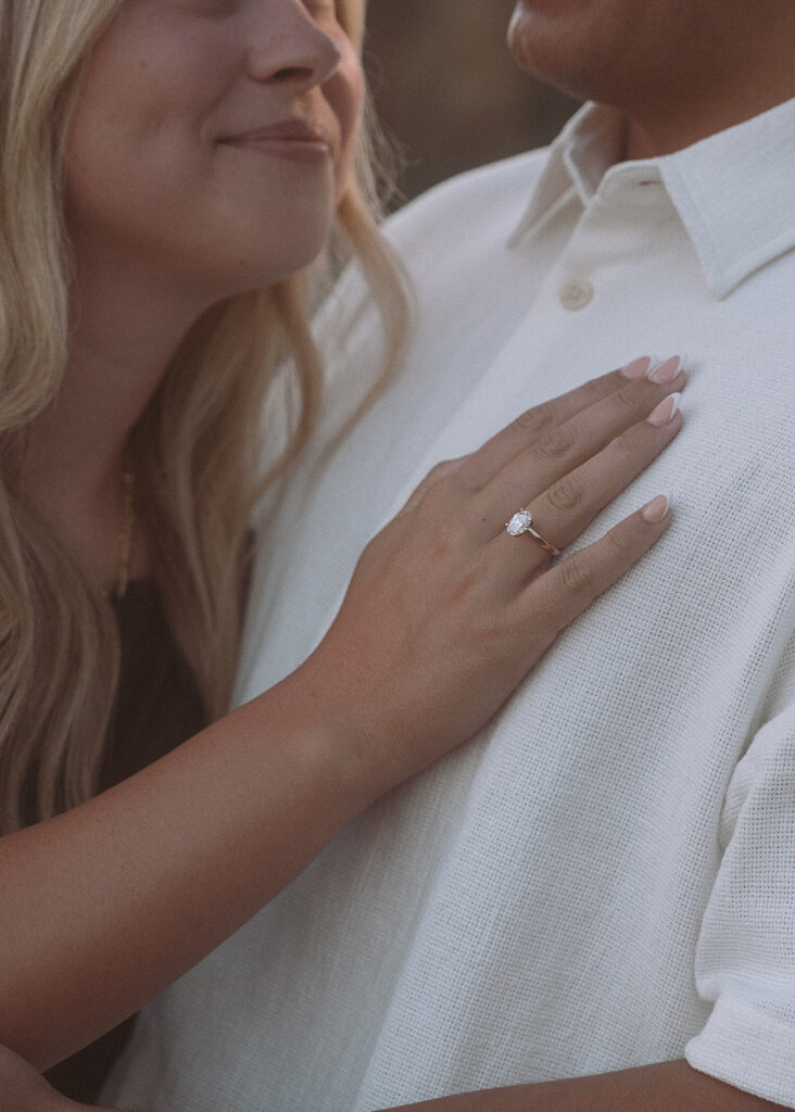 Close-up of a woman's hand with a new engagement ring resting on her fiancé's chest.