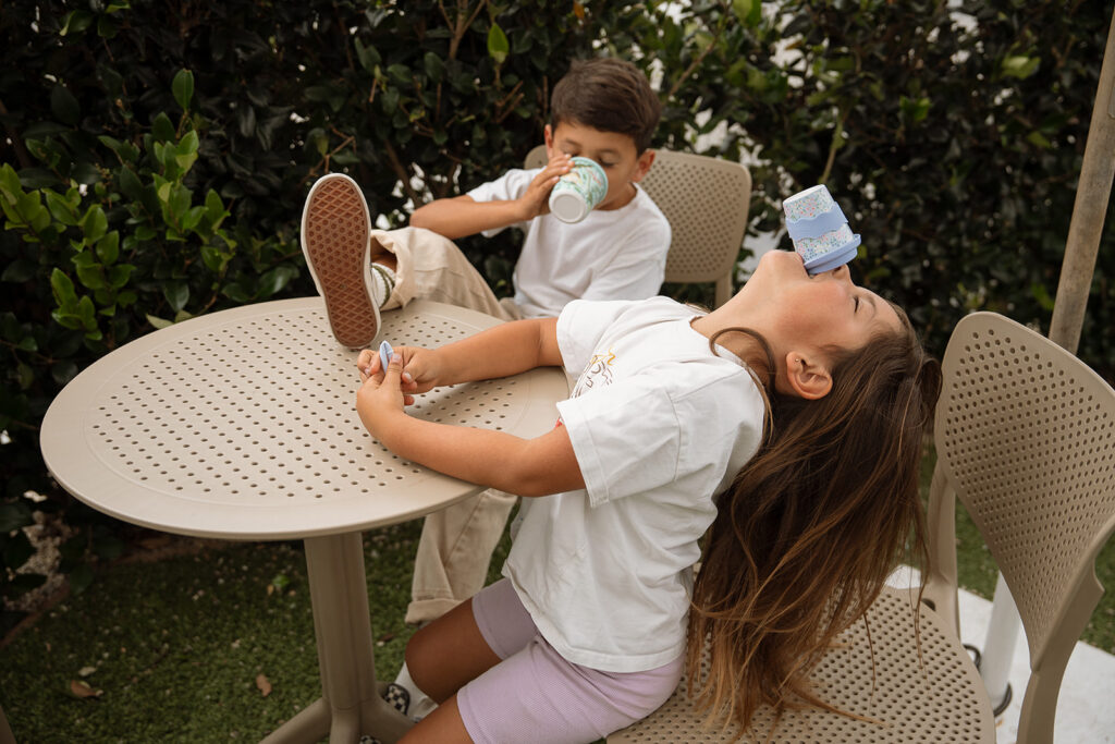 Siblings sitting outdoor cafe table with reusable cups