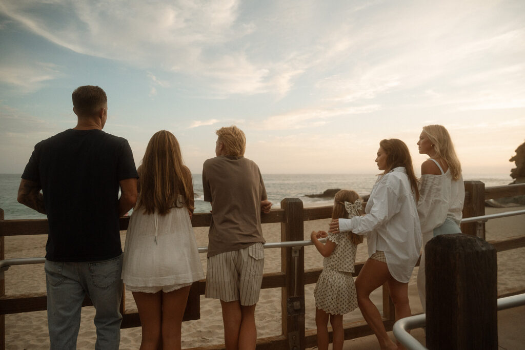 A family of six leaning on a wooden fence at sunset, looking out over the beach in Laguna Beach.