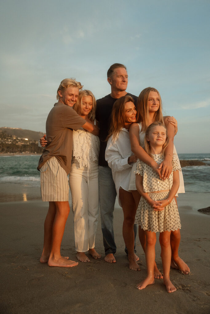 A family of six standing close together in golden evening light on the beach in Laguna Beach.