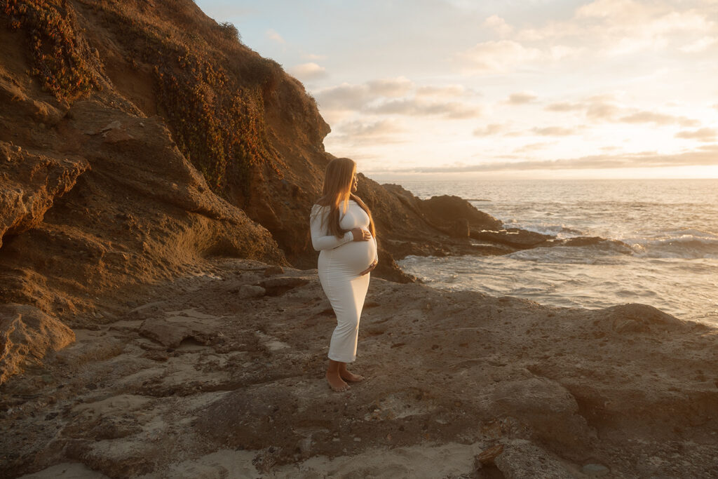 Pregnant mother standing on the ocean cliffs at sunset during a maternity photo session in Laguna Beach.