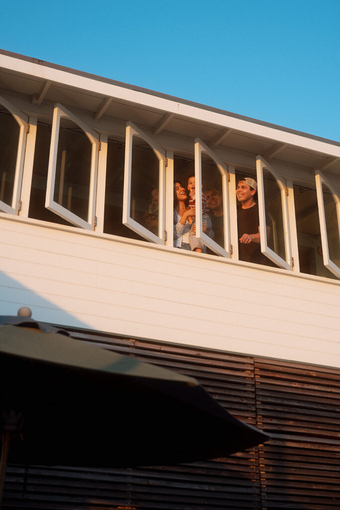Family laughing together through a row of open windows at a historic Crystal Cove beach cottage at golden hour.
